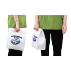A person wearing a green shirt and black pants holds a white paper bag with blue text BANGBANG JEANS 1961 and an illustration of a car. The bag is shown from the front and side, and the person has a bracelet on one wrist.