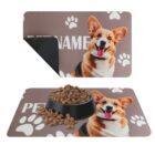 Two pet mats with a corgi image; one mat is plain, and the other has a black food bowl and kibble on it. Both mats have paw prints and the placeholder text PET NAME.