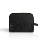 A black toiletry bag with a small white logo tag on the front. The bag has a simple design with a rectangular shape and a side handle. The background is a plain white surface.