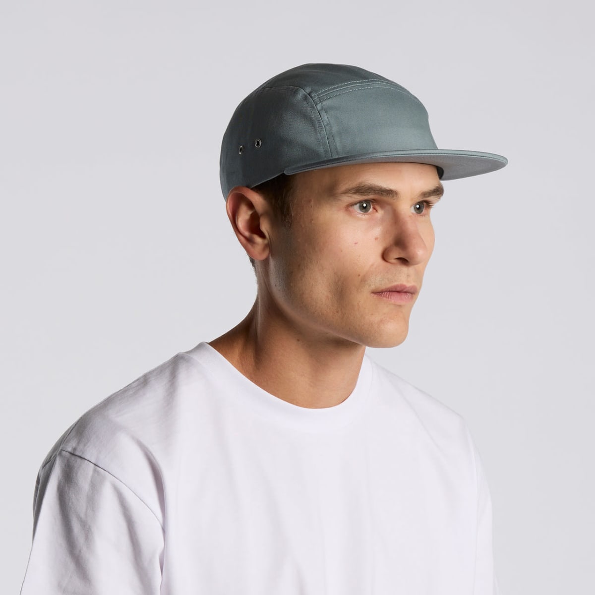 A person wearing a light gray baseball cap and a white T-shirt is looking to the left against a plain gray background.