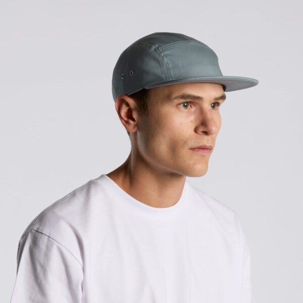 A person wearing a light gray cap and a white T-shirt is looking to the right against a plain light gray background.