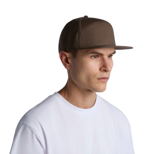A man wearing a brown flat-brimmed cap and a white t-shirt, staring to the right against a white background.