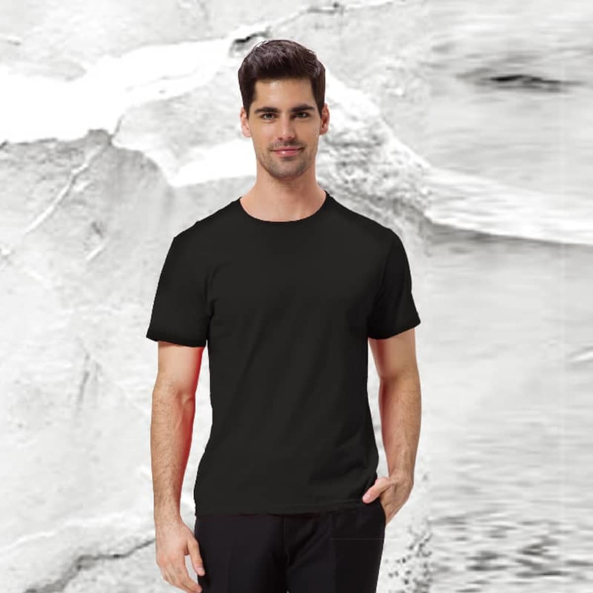 A man wearing the Essential Tee in black stands against a textured black and white background, with one hand in his pocket.