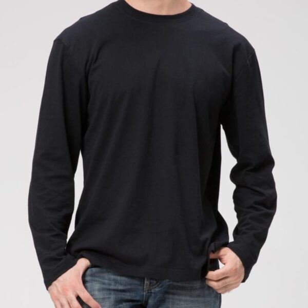 Wearing a Signature L/S Tee in black and blue jeans against a light gray background, they stand with one hand in their pocket, head slightly turned to obscure their face.