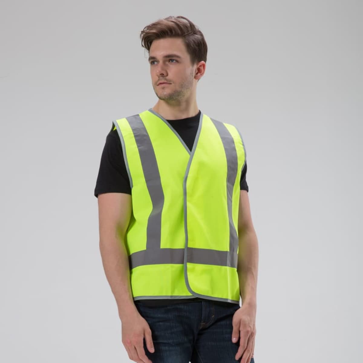 A person in a bright yellow VividReflect Vest stands against a plain background. The reflective gray stripes shine prominently, paired with a black shirt and jeans, combining style and safety.