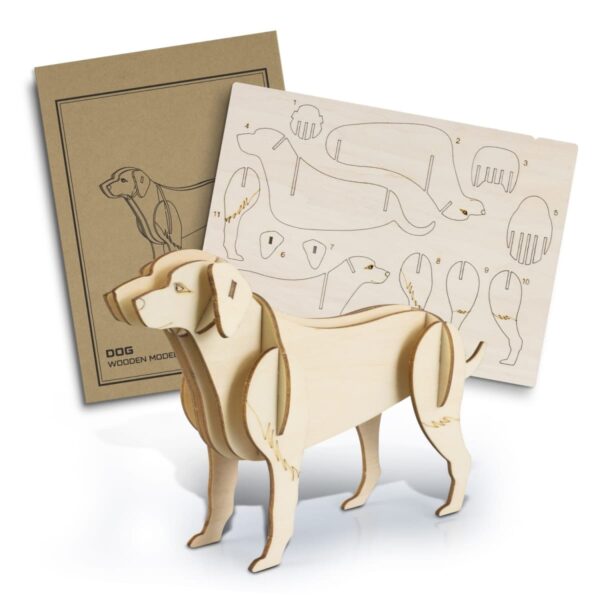 A wooden dog model completed and standing in front of assembly instructions and a sheet of parts. The instructions depict the outline of a dog, and the sheet shows laser-cut wooden pieces.