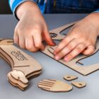 Child assembling a wooden puzzle on a table, focusing on fitting pieces together. The puzzle pieces are shaped like animal parts, and the childs hands are actively engaged in the assembly process.