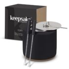Black container with a silver lid, next to two metal roasting sticks with black handles. A black and brown box labeled keepsake collection stands behind them.