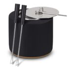 A black fondue set with a stainless steel lid and two fondue forks with black handles. The set has a modern, sleek design with a cork bottom, and the lid has a simple, curved handle.