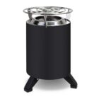A cylindrical black stove with metallic accents stands on three sturdy legs. The top features a circular metal grate. The design appears compact and modern, suitable for outdoor or portable use.