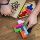 Children assembling colorful wooden puzzle pieces on a wooden floor, with a game box nearby.