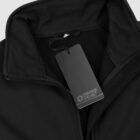 Close-up of a black jacket with a visible zipper, featuring a blank tag attached. The tag has a Swiss Peak logo embossed on it. The collar of the jacket is raised, and the fabric appears smooth and durable.