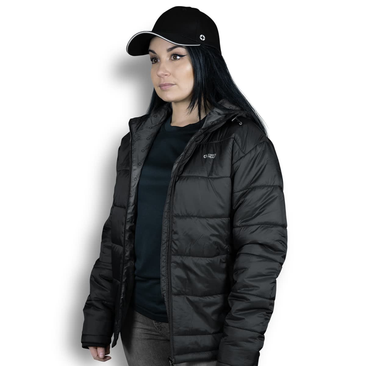 A person wearing a black cap and a puffy black jacket is standing against a white background. The person has long, dark hair and is looking to the side.