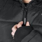 A person wearing a black puffer jacket, seen from the chest up, is shown adjusting the zipper. Their right hand is positioned on the zipper pull, and they have an engagement ring on their finger.