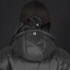 A person wearing a black puffer jacket with the hood raised is seen from behind. They have on a black baseball cap with an adjustable strap, and there is a small logo on both the jacket hood and cap. The background is solid dark gray.