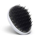 A round black scalp massager with a white edge, covered in numerous short, flexible bristles, angled in an upright position.