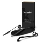 A black candle accessory set featuring a wick trimmer, snuffer, and wick dipper is arranged in front of a sleek, branded black box. The tools have a modern design and are displayed on a matching black tray.