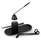 A black candle on an oval tray is surrounded by a candle snuffer, wick trimmer scissors, and a wick dipper. The candle is lit, and the tools are neatly arranged, all in a modern, minimalist style.