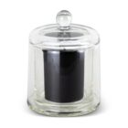 A black candle in a glossy black glass jar is placed inside a clear glass cloche with a rounded handle on top. The cloche highlights the candles minimalistic and elegant design.