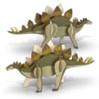 Two 3D stegosaurus puzzles made of cardboard are assembled and standing side by side. The models feature green bodies with brown and beige plates along their backs and tails, set against a white background.