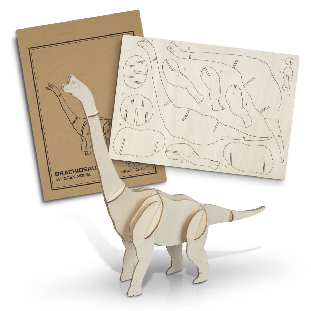 A wooden Brachiosaurus model kit with assembly instructions is displayed. The kit includes several pieces on a wooden board, partially assembled, with the completed dinosaur model standing beside it.