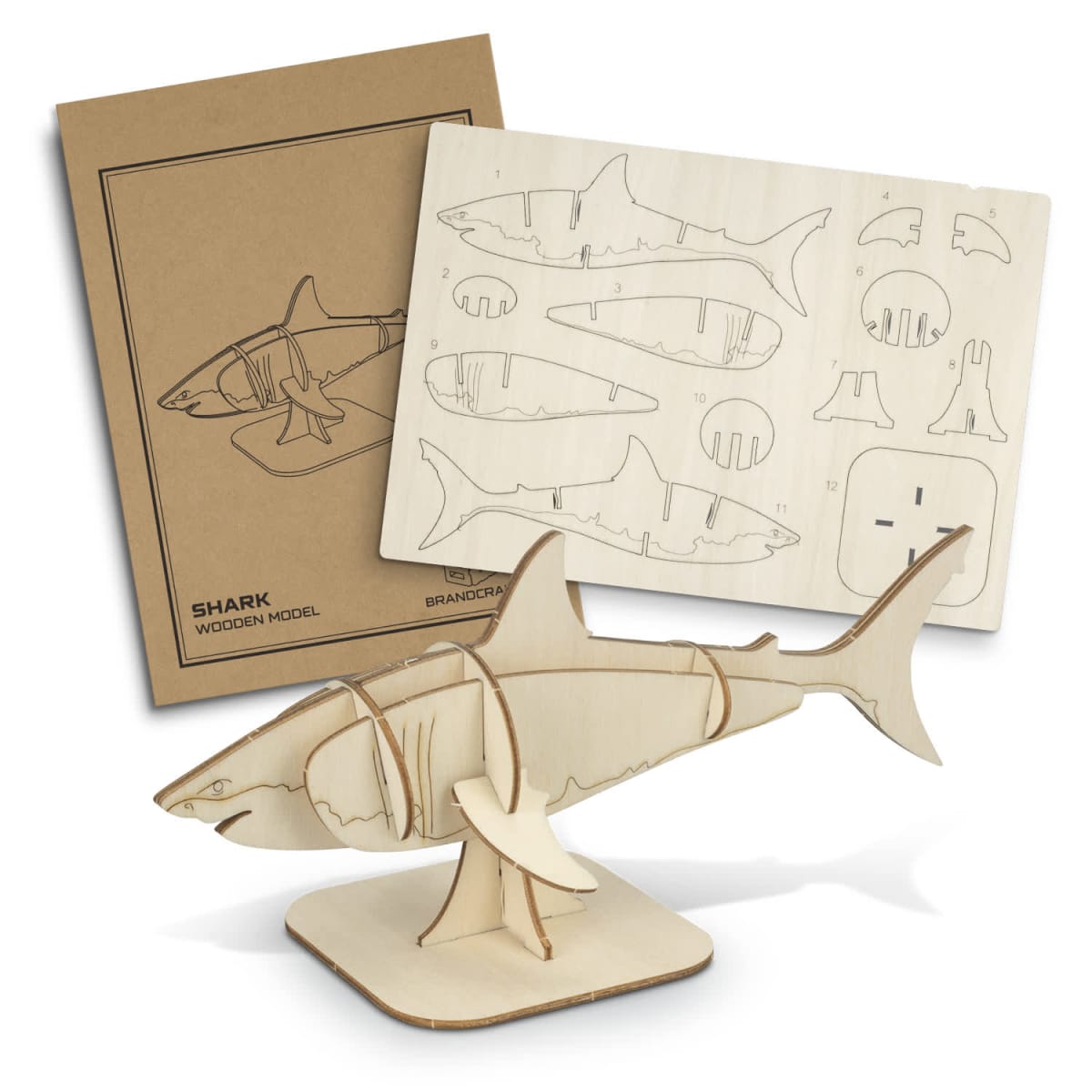 A DIY wooden shark model kit is shown with assembled and disassembled pieces. The completed model is mounted on a stand, while the disassembled parts are laid out on a sheet. Instructions are visible in the background.