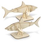 Two wooden shark models are displayed, each assembled from light-colored, interlocking pieces. They stand upright on flat bases, showcasing detailed cutouts and natural wood texture.