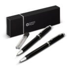 A sleek black and silver Swiss Peak pen set is displayed, featuring a ballpoint pen and a rollerball pen. Accompanying the pens is a black rectangular case and an extra ink refill, all set against a white background.