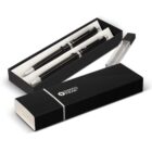 A black gift box with a silver logo, containing two elegant black pens with silver accents. One pen is displayed outside the box, while the other is inside. The box lid is placed beside it.