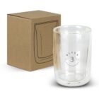 A clear double-walled glass with Black Cafe Lounge logo sits next to a brown cardboard box with a black line illustration of the glass on its side. The glass has a modern design and is empty.