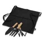 A set of gardening tools, including a trowel, a fork, and a hand cultivator with wooden handles, is placed on a black canvas apron with straps.