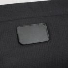 A close-up of a textured black rectangular patch on a dark fabric surface, possibly a label or badge. The texture appears slightly grainy, with fine horizontal lines visible on both the patch and fabric.