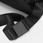 Close-up of a black strap with a rectangular plastic buckle on a light background. The strap is angled, showing a textured fabric and an adjustable length mechanism.