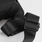 Close-up of a black fabric strap with a black metal buckle, placed against a white background. The strap features textured lines, adding detail to its appearance.