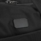 Close-up of a black backpack featuring a textured surface with a small rectangular patch and shiny metal zippers. The fabric has a grid-like pattern, adding to its rugged appearance.