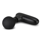 A black handheld percussion massager featuring a round attachment lies on a plain white background. The device has a sleek, ergonomic design, and is positioned at an angle, highlighting its compact and portable structure.