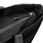 Close-up of a black bags zippered pocket with a sturdy zipper pull and a textured fabric. The zipper is partially open, revealing the interior lined with dark material. The bag has a sleek, simple design.