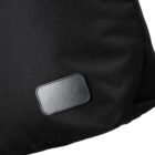 Close-up view of a black textured fabric with a small rectangular gray patch sewn onto it. The fabric appears to be part of a bag or clothing item.