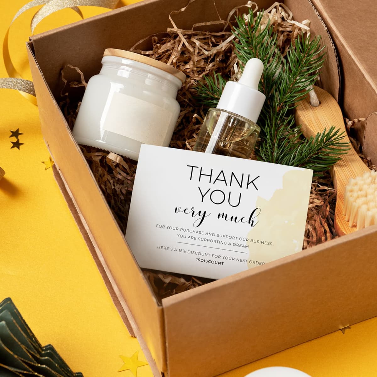 A gift box with a candle, dropper bottle, small wooden brush, and a pine branch. A thank you card inside reads, THANK YOU very much along with a discount code. The background is decorated with stars and ribbons.
