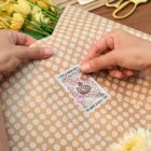 Hands sealing a polka dot envelope with a sticker that says, Its a good day to have a good day. Yellow flowers and scissors are in the background.
