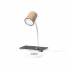 A modern desk lamp with a cork-textured shade and a flexible white neck. The base features a wireless phone charging pad with a smartphone on it, displaying a charging icon. A power cable extends from the base.