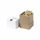 A brown box partially opened to reveal a small bottle inside, next to a closed white box on a white background. A card is visible inside the brown box lid.