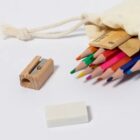 A collection of colored pencils partially inside a drawstring pouch on a white surface. Nearby are a wooden pencil sharpener, a white eraser, and a wooden ruler.