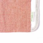 Close-up of a pink fabric bag with speckled texture, featuring a white drawstring and a small white tag with a green recycling symbol and the text RECYCLED COTTON.