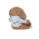 A plush teddy bear with brown fur is sitting and facing away, wearing a light gray hoodie. The bears head is slightly turned to the side and one ear is visible. The background is plain white.