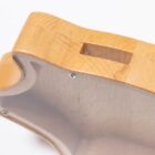 Close-up of a wooden guitar body frame, showing a cutout section and metal screws. The wood has a smooth, polished surface with a natural grain pattern, highlighted against a plain background.