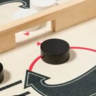 Close-up of a board game showing a black circular piece on a beige surface with red and black arrows. A wooden barrier separates black and white pieces, indicating game play movement and strategy elements.