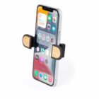 A smartphone with a visible home screen is held by a car vent mount featuring wooden grips. The mount is designed to securely hold the phone while driving.