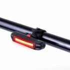 A red LED bike light attached to a black bicycle handlebar. The light is on, emitting a bright red glow. The background is a plain white.