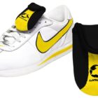 A white sneaker with a yellow swoosh, accompanied by a black and yellow tongue cover labeled Wavehog. The cover protects the shoes laces and is shown separately for detail.
